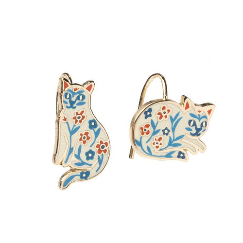 Mismatched enamel drop earrings featuring white cats decorated with folk-style blue and red floral illustrations by Yellow Owl Workshop