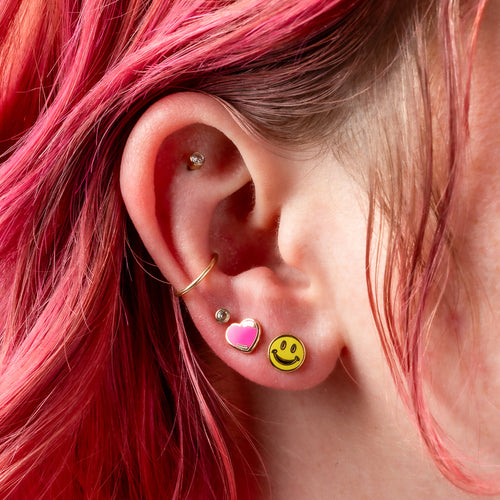 Happy Face and Heart mismatched gold stud earrings worn on ear by Yellow Owl Workshop