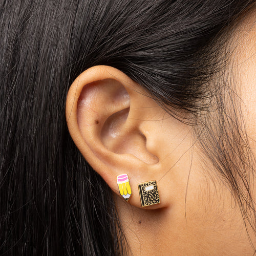 Pencil and Notebook mismatched gold stud earrings worn on ear by Yellow Owl Workshop