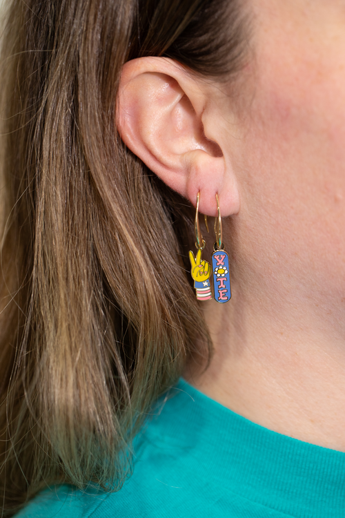 Mismatched enamel drop earrings featuring blue Vote badge with daisy and pink and blue peace sign hand by Yellow Owl Workshop