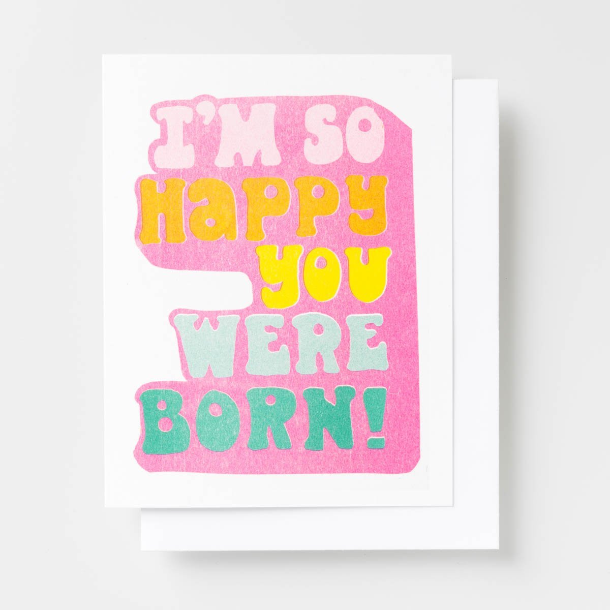 Risograph greeting card with bold retro typography in pink, yellow, and teal reading I'm So Happy You Were Born on a hot pink background